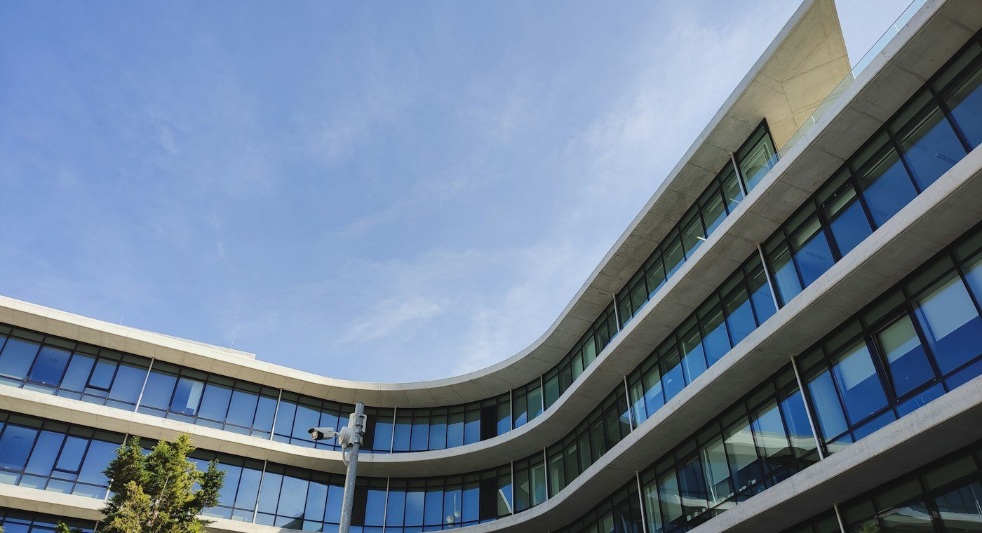 Modern glass-fronted office building with curved facades under a blue sky