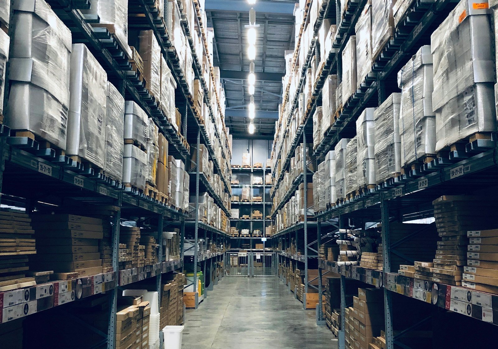 Long aisle in a modern distribution warehouse with tall racks of palletised cartons under bright industrial lighting