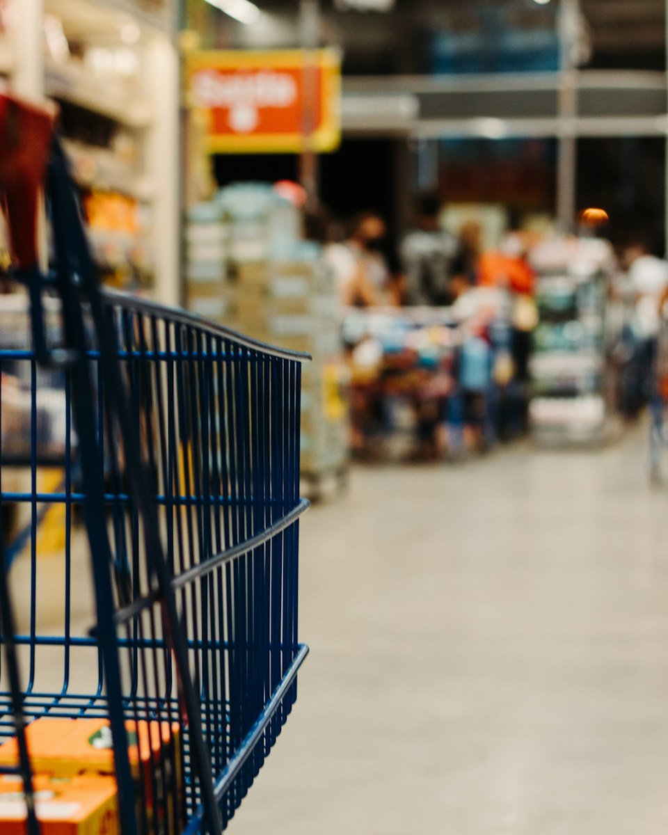 Shopping trolley in a busy supermarket aisle stocked with consumer products